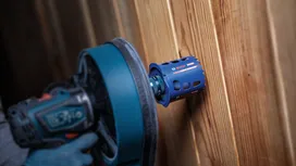 Une personne portant un équipement de sécurité perce un trou dans un mur en bois.